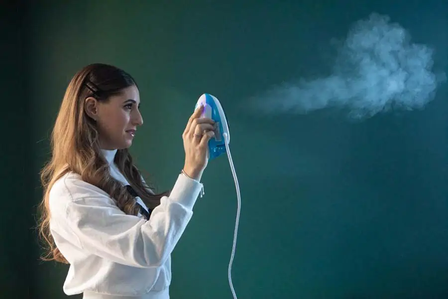 Melissa Maker holding a clothes steamer shooting steam