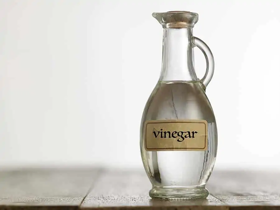 A glass jar labelled vinegar sitting on a wooden table.